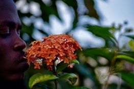 A smiling person gently spraying perfume on their wrist, surrounded by delicate blossoms.