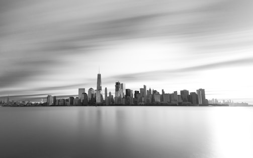 A serene black-and-white photograph of a misty urban skyline at dawn, with soft light filtering through.