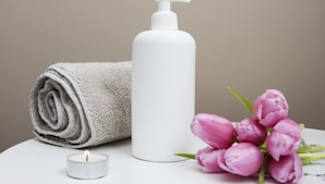 white plastic pump bottle beside pink tulips and gray towel