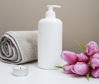 white plastic pump bottle beside pink tulips and gray towel