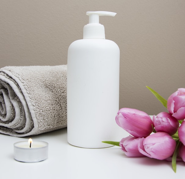 white plastic pump bottle beside pink tulips and gray towel