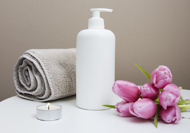 white plastic pump bottle beside pink tulips and gray towel