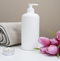 white plastic pump bottle beside pink tulips and gray towel