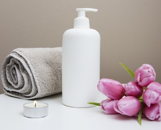 white plastic pump bottle beside pink tulips and gray towel