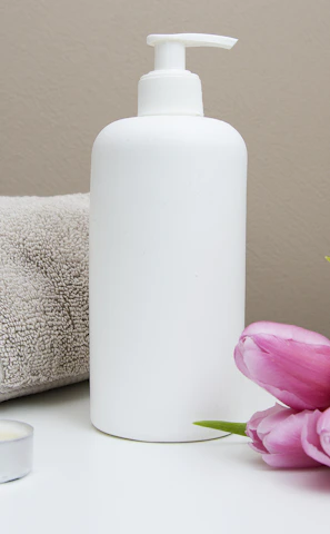 white plastic pump bottle beside pink tulips and gray towel