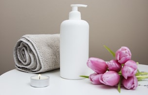 white plastic pump bottle beside pink tulips and gray towel