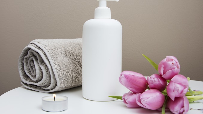 white plastic pump bottle beside pink tulips and gray towel