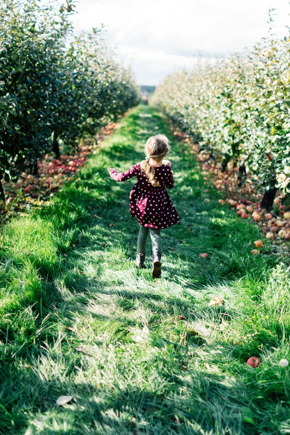 Ragazza che indossa un vestito a pois marrone e bianco che corre sul campo del sentiero in erba