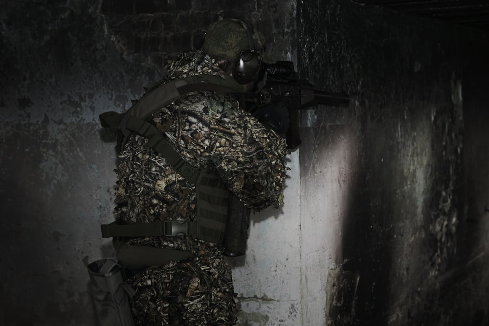 a man in camouflage holding a rifle in a dark room