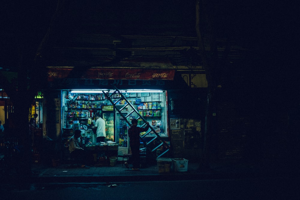 man carrying ladder in front open store at night