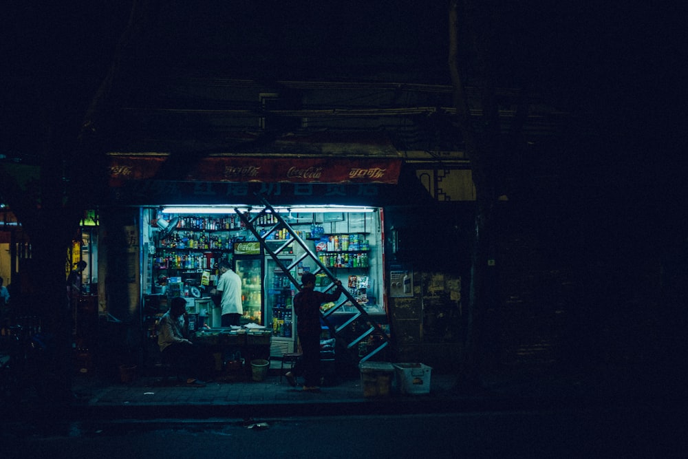 hombre que lleva la escalera en la tienda abierta al frente por la noche