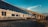 A high-speed passenger train is seen traveling along a railway track adjacent to a concrete bridge under a clear blue sky. The train has a sleek design and is moving rapidly, creating a sense of motion. The scene includes a mix of natural landscape with flora visible in the foreground.