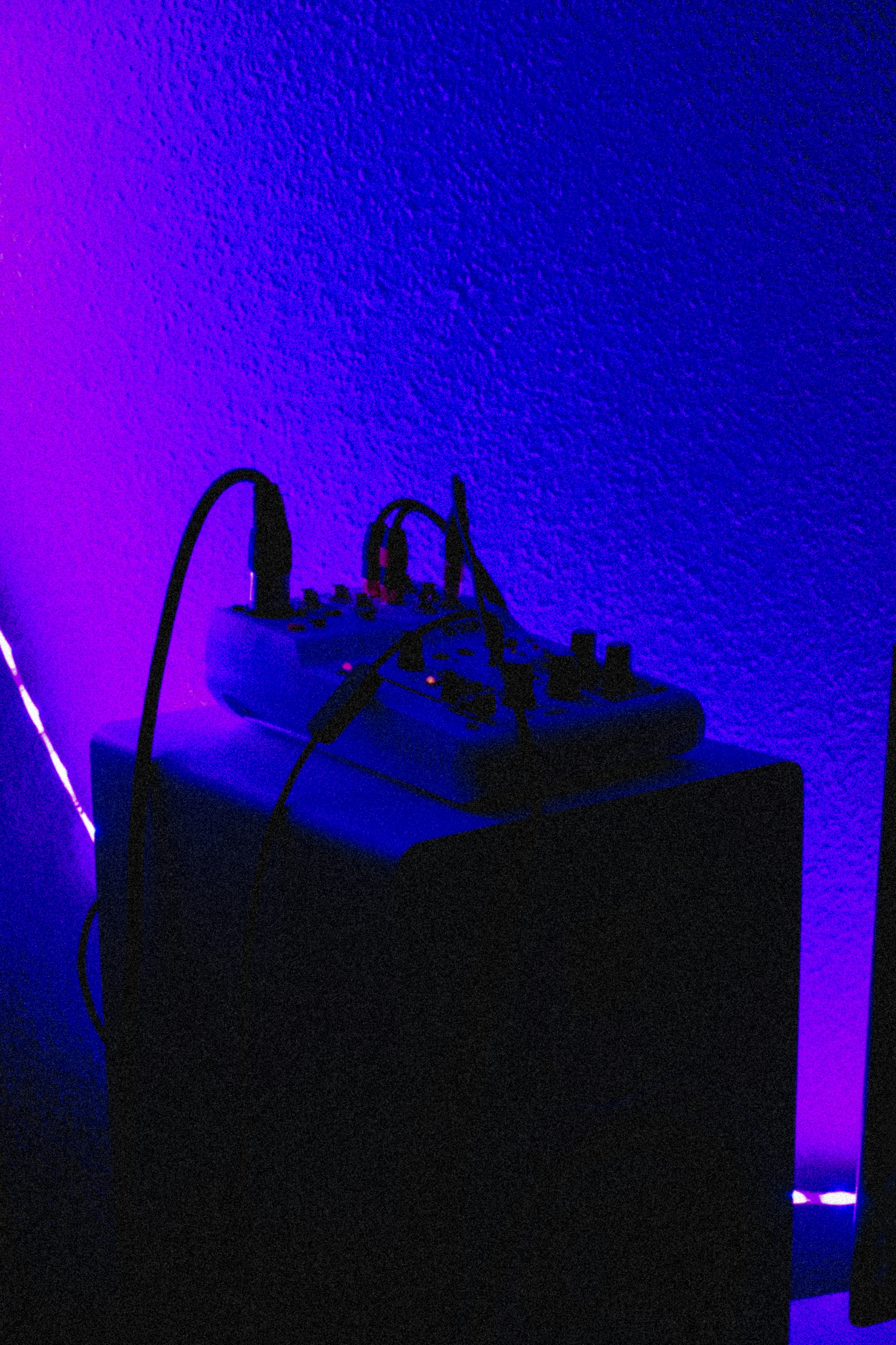 Music studio with professional audio equipment glowing in dark blue and purple light, mixing board in foreground
