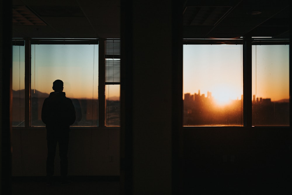 Silhouette einer Person, die während der goldenen Stunde vor dem Fenster steht