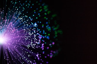 A burst of colorful lights resembling fiber optics with vibrant purples, blues, and greens against a dark background.