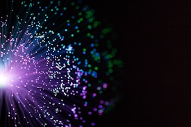 A burst of colorful lights resembling fiber optics with vibrant purples, blues, and greens against a dark background.