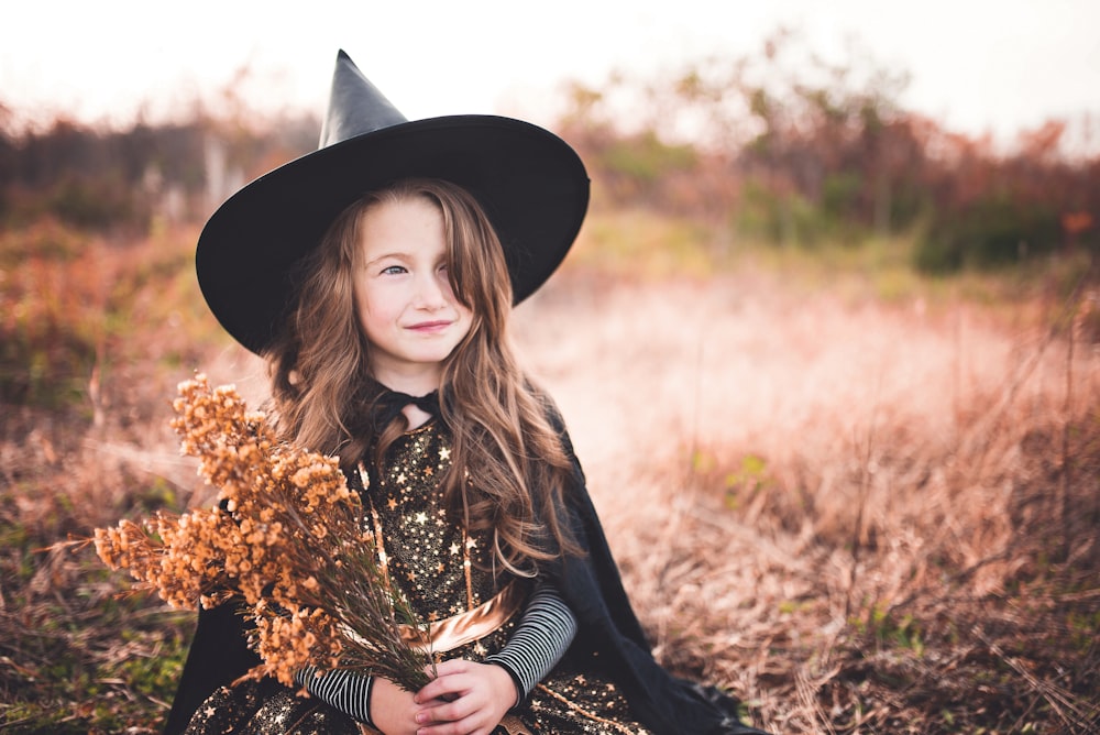 girl wearing black witch costume holding brown plant