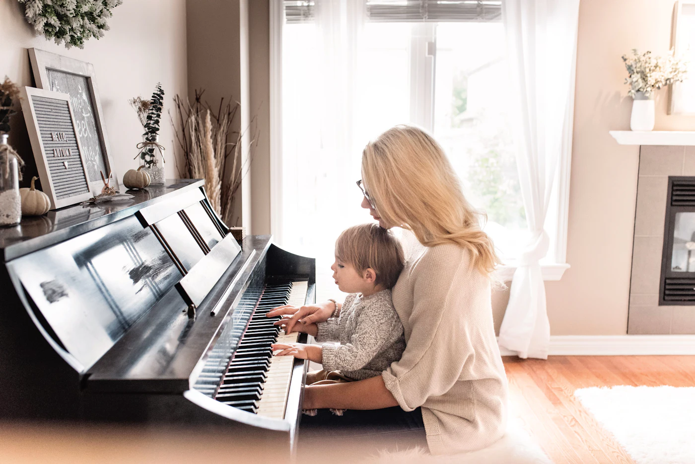 An adult and a young child at an upright piano in a living room