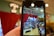 A phone held in the foreground captures a vibrant toy store display. The store features shelves filled with a variety of toys, including stuffed animals and boxes of games. Above the display, a bright marquee sign spells 'Toys' against a backdrop of red curtains.