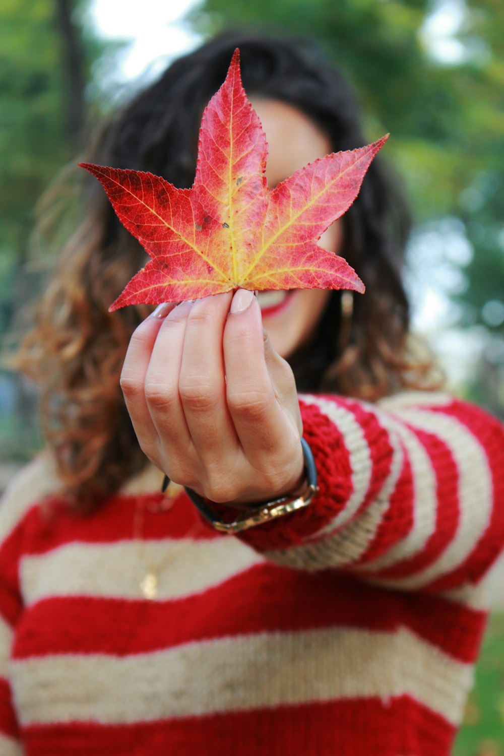 woman holding red maple leaf covering her face