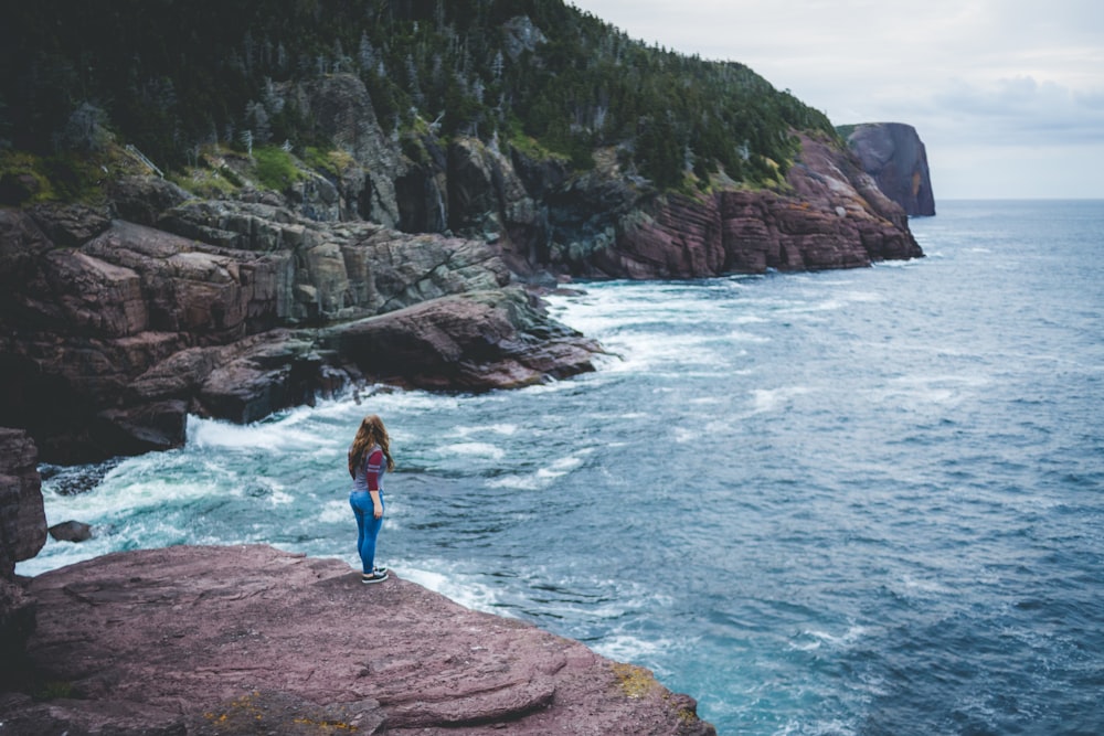 a woman standing on top of a cliff next to the ocean