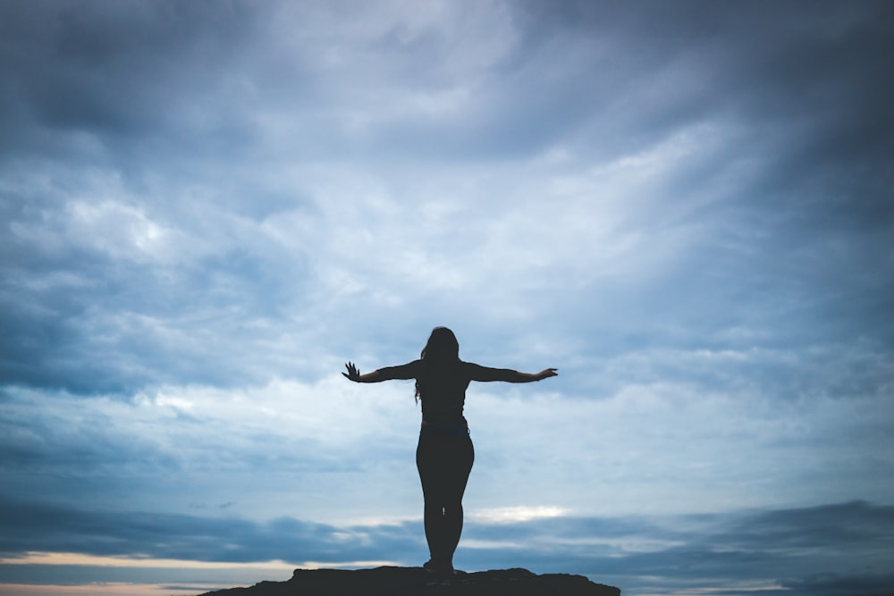 Silhouettenfotografie einer Frau, die auf einem Felsen steht