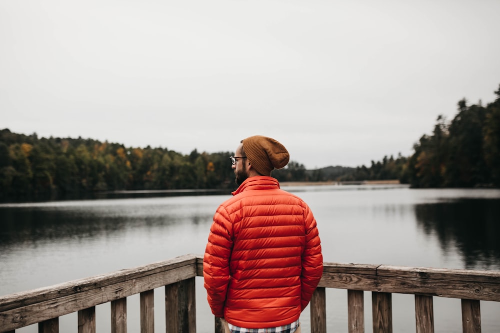 man standing near brown wooden balustrade facing body of water