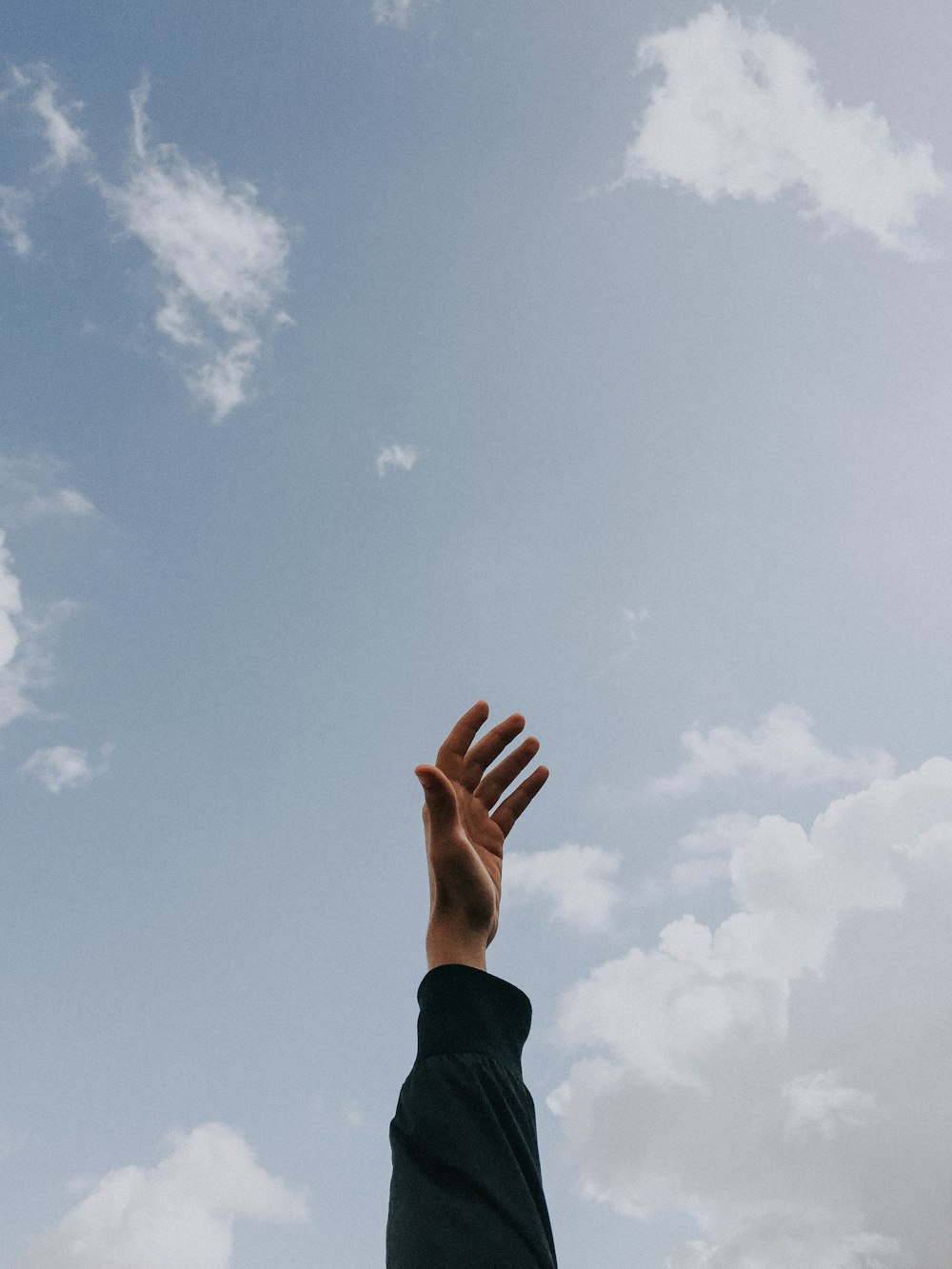 person raising left hand under cloudy sky at daytime