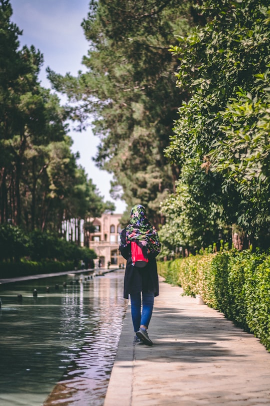 woman in black top walking by hedge and body of water in Yazd Province Iran