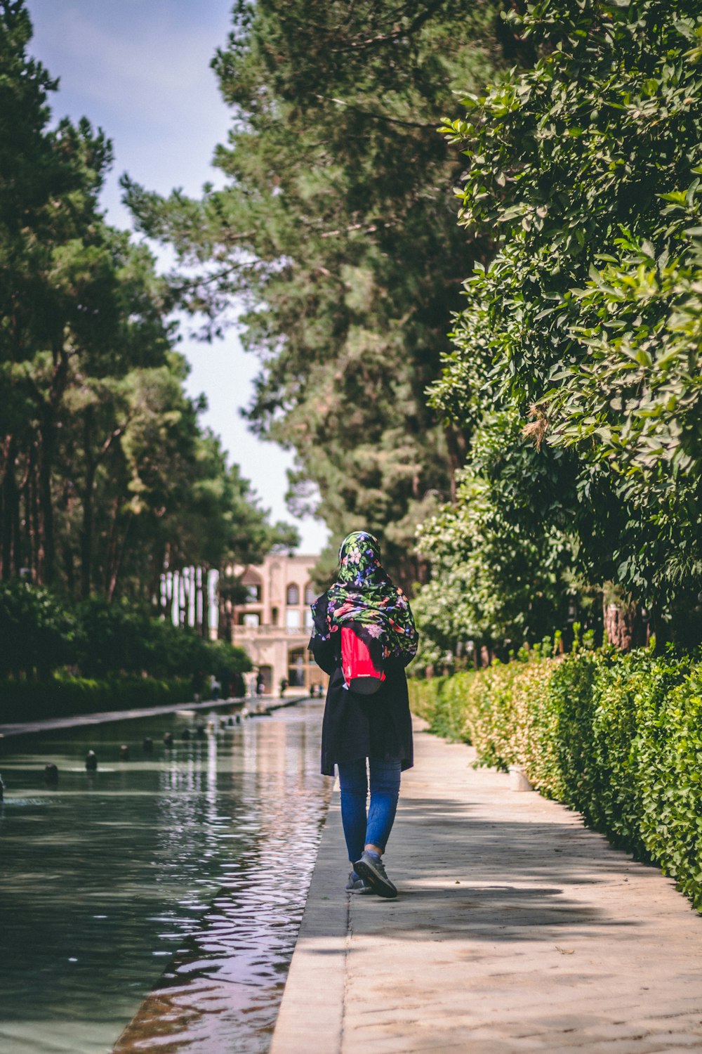 Donna in top nero che cammina dalla siepe e dallo specchio d'acqua