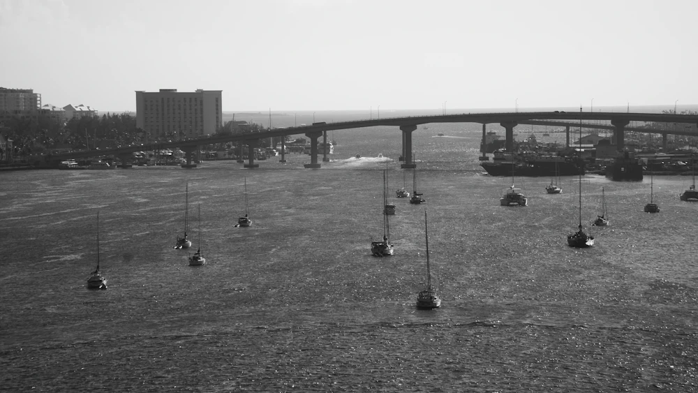 Black-and-white aerial photograph of sailboats moored in Nassau harbour, Bahamas, with a bridge crossing the water, no people visible