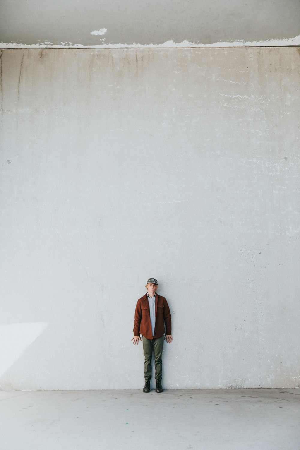 man in brown coat standing by the white wall