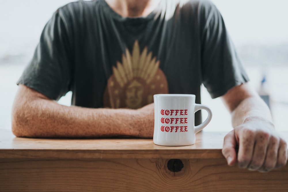 man in green and brown t-shirt sitting by the bar table with white coffee mug