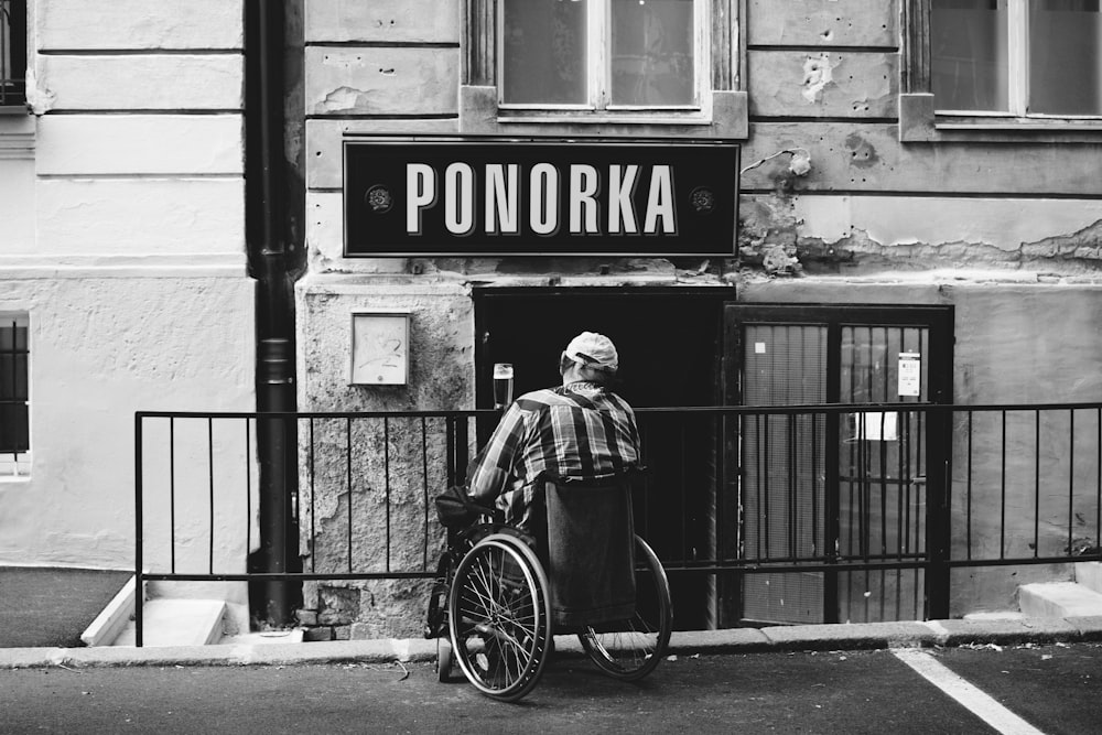 Ponorka 간판을 보고 있는 휠체어를 탄 사람의 회색조 사진