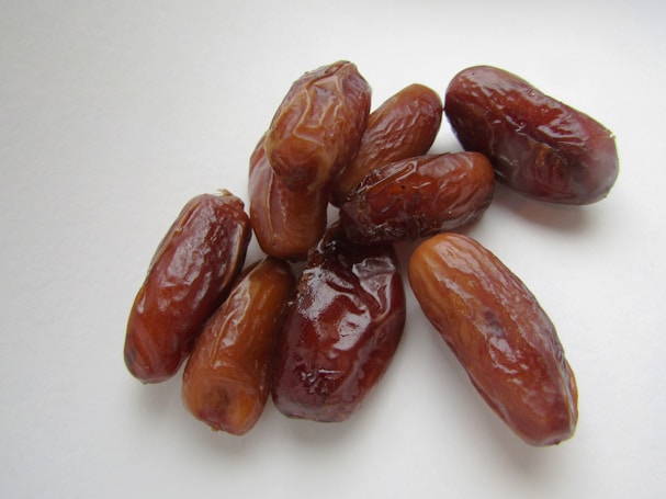 A cluster of shiny, reddish-brown dates arranged on a white background, showcasing their wrinkled textures and elongated shapes.