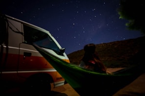 A lightweight camping hammock setup with an attached mosquito net under a starry night sky.