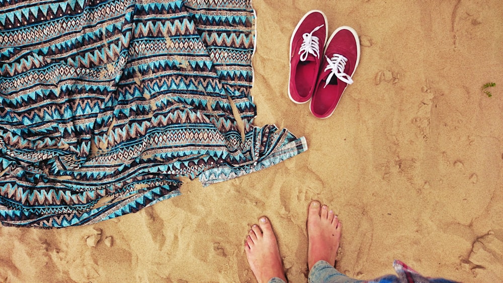 person standing on sand beside red low-top shoes