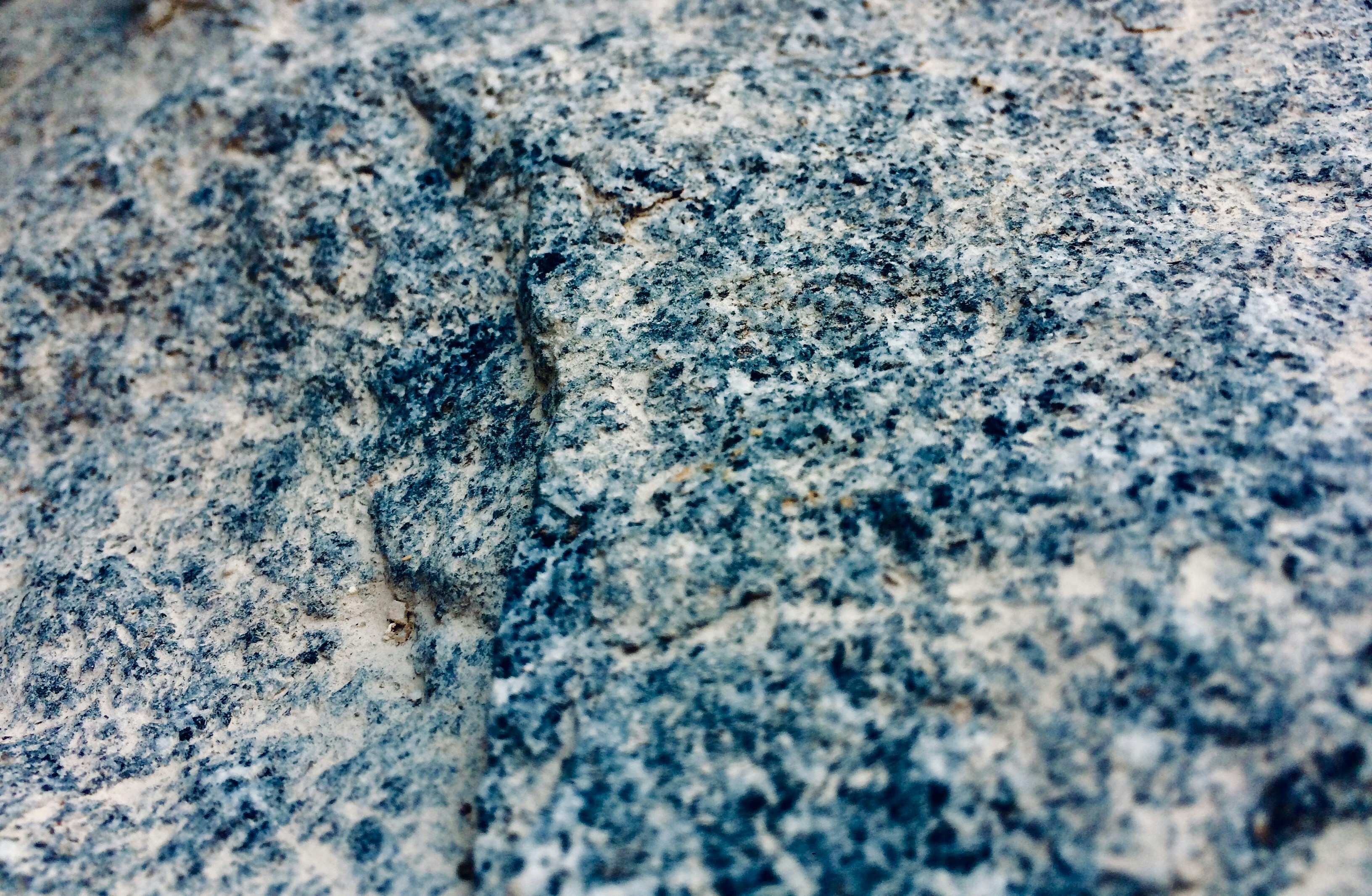 A close-up view of a granite rock surface displaying a rough, textured appearance with a mixture of blue, gray, and white colors.
