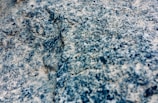 A close-up view of a granite rock surface displaying a rough, textured appearance with a mixture of blue, gray, and white colors.