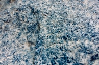 A close-up view of a granite rock surface displaying a rough, textured appearance with a mixture of blue, gray, and white colors.