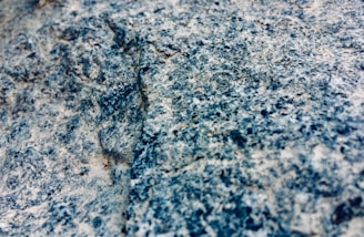 A close-up view of a granite rock surface displaying a rough, textured appearance with a mixture of blue, gray, and white colors.