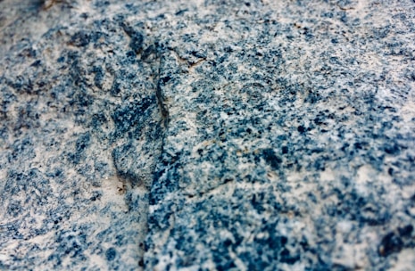 A close-up view of a granite rock surface displaying a rough, textured appearance with a mixture of blue, gray, and white colors.