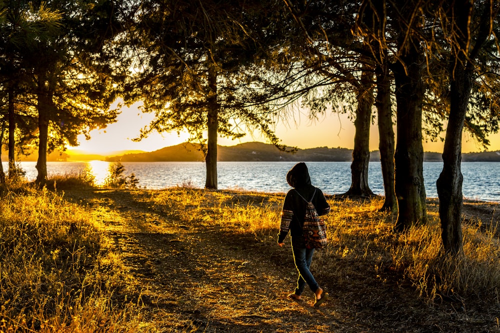 woman walking under trees near body of water