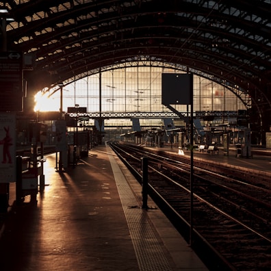 An old wooden train station bathed in golden morning light with a lone traveler waiting.