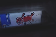 A cartoon-like drawing features a red animal with a large head and four legs, possibly depicting a pig or a whimsical creature. To the left, there is a blue object with white outlines that might resemble an abstract piece or part of a larger illustration.