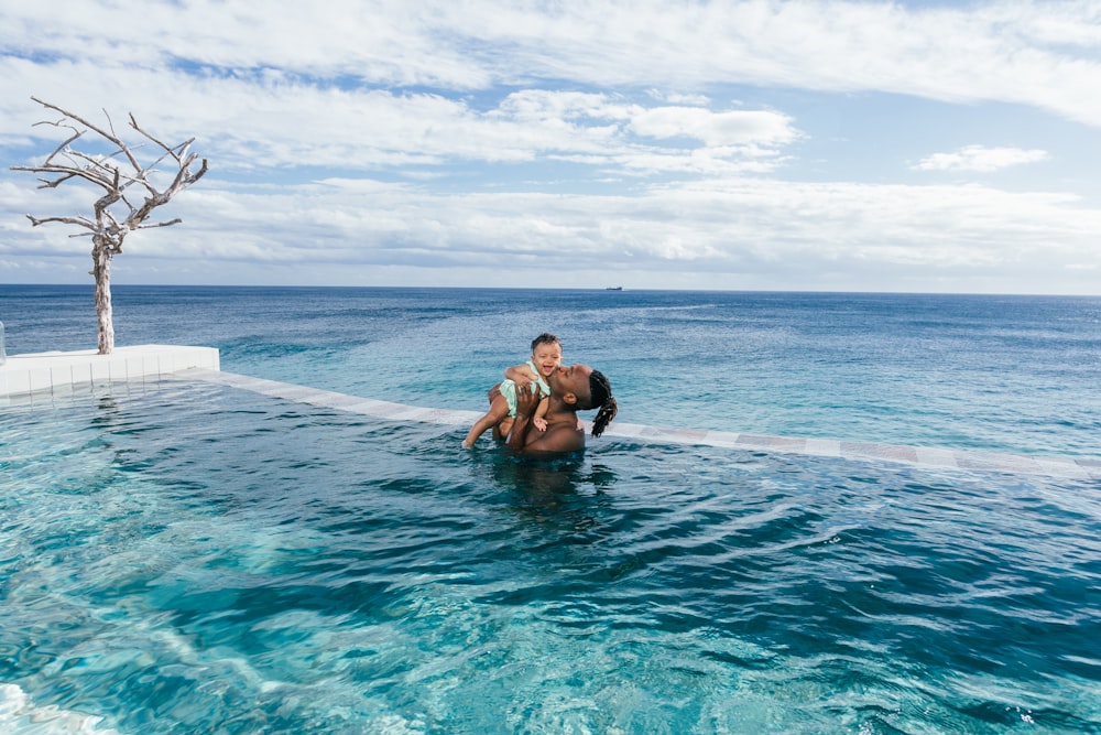 man carrying baby while standing on infinity pool