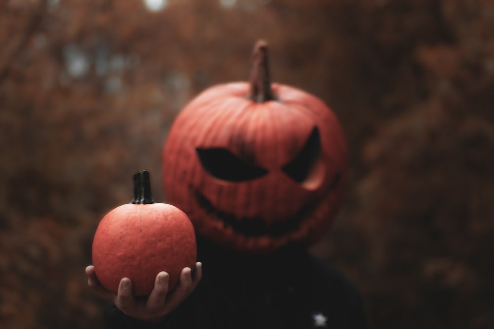 person wearing Jack-O-Lantern mask holding pumpkin