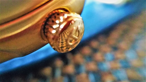 Macro photo of a watch crown with engraved logo and fine knurling.