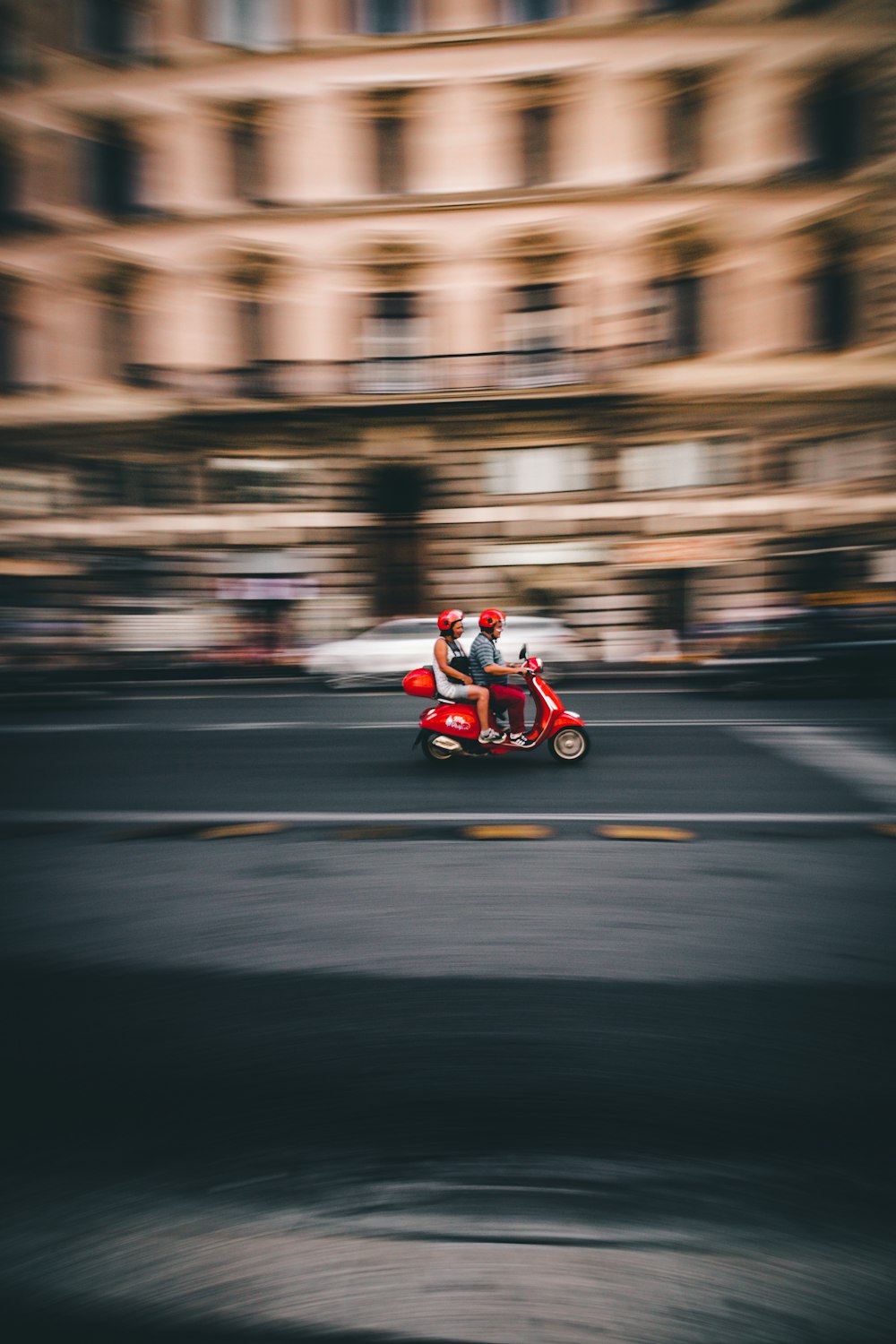 panning photography of two person riding red motor scooter