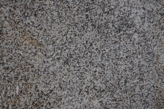 A close-up of a textured granite surface featuring a mix of gray, black, and subtle brown speckles.